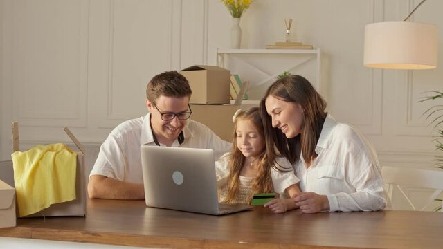 A Happy Family Uses a Laptop for Online Shopping, Sitting at Home. Parents With Child Use a Credit Card for Online Shopping. Buying by the Internet. A Familly to Сonnecting With Online Shopping.