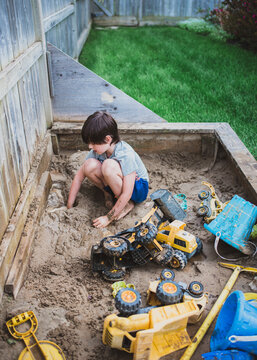 Young boy playing in muddy sandbox in backyard filled with toys.