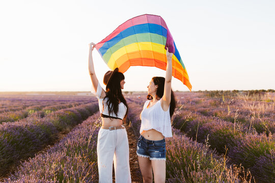 Girlfriends looking each other in a lavender field waving a lgbt flag