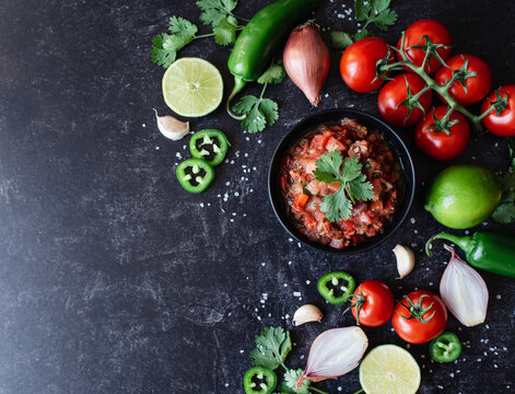 Bowl of fresh salsa with the ingredients and on black slate counter.