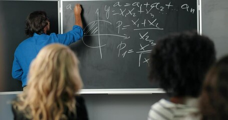 Rear on Caucasian male teacher writing math laws and formulas on blackboard in classroom. Back view on man lecturer explaining mathematics or physics to students. University study.