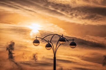 Street lamp on the background of the sunset sky with the silhouette of the sun