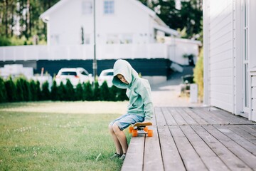 young boy sat on a skateboard on his own at home
