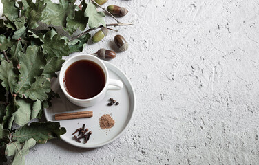 Cup of acorn coffee, acorns and green oak leaves on a gray background. An alternative to...