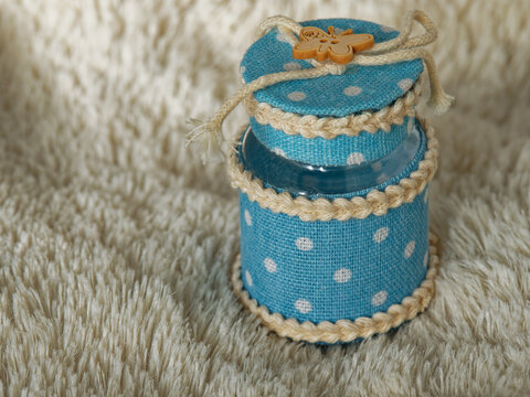 Handmade gift items. A box for sugared almonds made with a clear glass jar, light blue fabric with floral motifs and a small wooden butterfly.