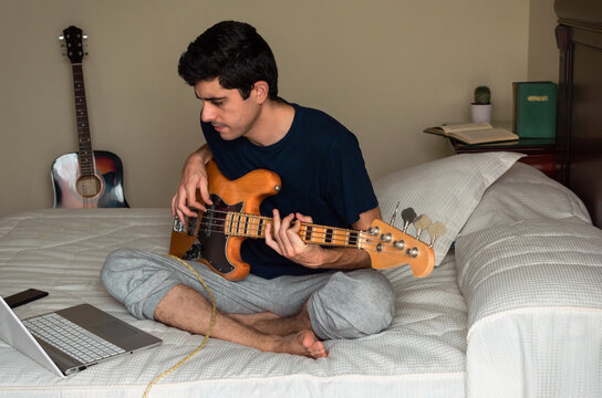 Young man learning to play the electric bass using a computer at home.