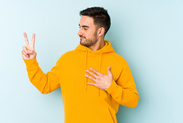 Young caucasian man isolated on blue background taking an oath, putting hand on chest.