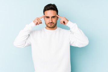 Young caucasian man isolated on blue background focused on a task, keeping forefingers pointing head.