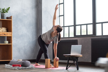 Sporty young woman practicing yoga, doing Revolved Triangle Pose, Parivrrta Trikonasana, working...