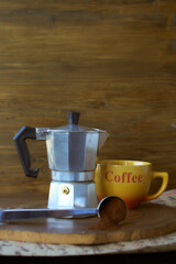 Geyser coffee maker on a wooden tray. There's a cup of coffee next to it. Dark background