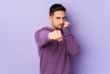 Young caucasian man isolated on purple background throwing a punch, anger, fighting due to an argument, boxing.