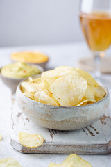Crunchy delicious potato chips in a bowl with beer for a tasty snack break on light background