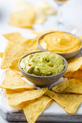 Nachos chips in a bowl with sauces guacamole and cheese, dip variety, over white stone background.