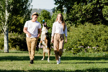 Young and modern couple walking and playing with their dog Border Collie in a park
