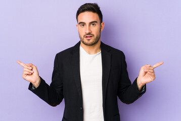 Young caucasian man isolated on purple background pointing to different copy spaces, choosing one of them, showing with finger.