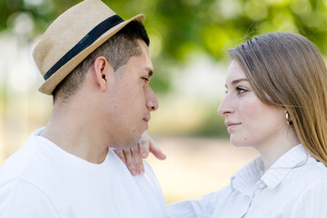 young couple looking into each other's eyes in a park. Latin man and Caucasian woman