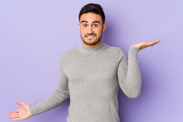 Young caucasian man isolated on purple background confused and doubtful shrugging shoulders to hold a copy space. - obrazy, fototapety, plakaty