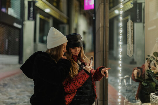 Portrait of two friends during shopping at city, looking at windows shop.