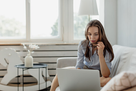 Portrait of young woman working at home, on sofa with computer, Minsk, Belarus.