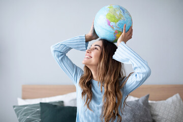 Cheerful young woman holding globe at home.