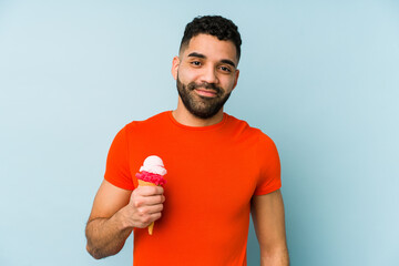 Young latin man holding an ice cream isolated happy, smiling and cheerful.