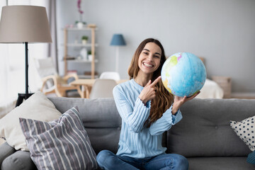 Young female tourist holding globe, pointing with index finger to desirable destination of her trip. Planning vacation.