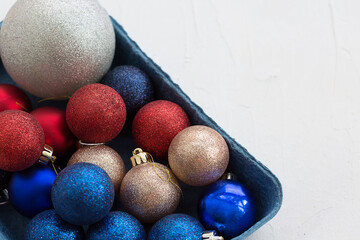 Set of multicolored Christmas tree decorations in a box close up on a white textured horizontal background.