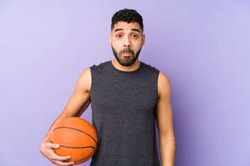 Young latin man playing basket isolated shrugs shoulders and open eyes confused.