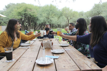 
group of people latin family with protection mask eating, drinking and toasting in outdoor...