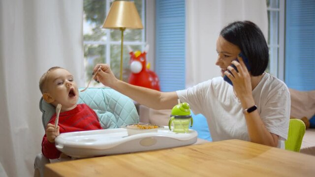 Busy mother on mobile phone feeding baby at same time