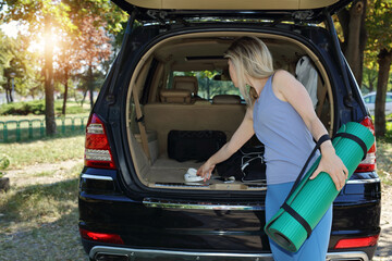 Sport woman getting ready for workout outdoor, taking exercise mat from car trunk