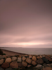 Fototapeta na wymiar Sunrise seascape over the rocky bank on an overcast morning at Falmouth Trunk Beach on Cape Cod