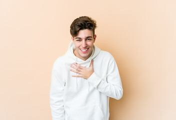 Young caucasian man isolated on beige background laughs out loudly keeping hand on chest.