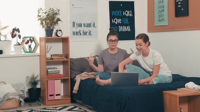 PAN Shot Of Happy Female Friends Sitting On Bed At Home Or In Dorm Room And Dancing To Music Together