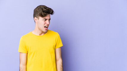 Young caucasian man isolated on purple background shouting very angry, rage concept, frustrated.