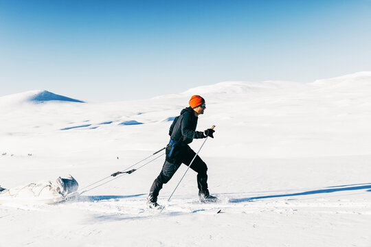 Male Skier Pulling Cargo Sled Through White Winter Landscape