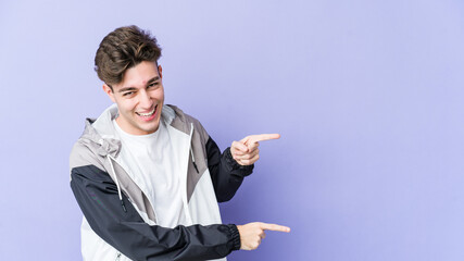 Young caucasian man isolated on purple background pointing with forefingers to a copy space, expressing excitement and desire.