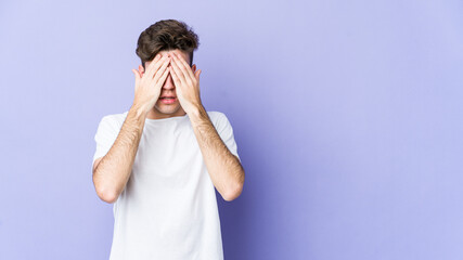 Young caucasian man isolated on purple background afraid covering eyes with hands.
