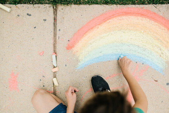 Young boy drawing sidewalk chalk rainbows