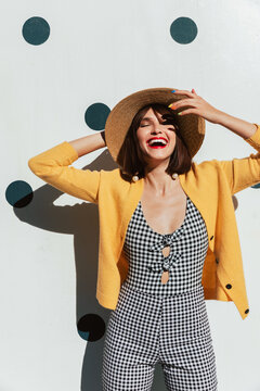 Young stylish woman laughs and poses in front of polka dot wall.