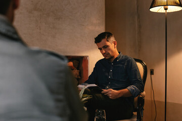 Middle-Aged Caucasian Man Reading Book by Fireplace