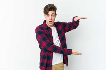 Young caucasian man isolated on white background shocked and amazed holding a copy space between hands.