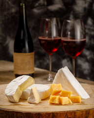 Vertical image with cheese camembert, brie, parmesan and wine on wooden board
