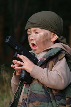 A Little boy soldier with a camouflage painted face and a gun