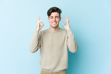 Young caucasian man isolated on blue background crossing fingers for having luck