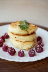 Juicy curd cheesecakes lie on a white saucer with raspberries and mint leaf. Light background