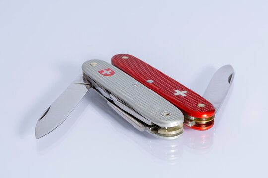 Silver and red half opened penknifes side by side with grey background