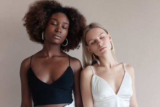 Sensual indoor portrait of two multiracial models posing together in stylish studio. Togetherness concept.