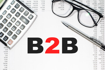 B2B in a magnifying glass on a notepad against the background of graphs, calculator and paper clips.
