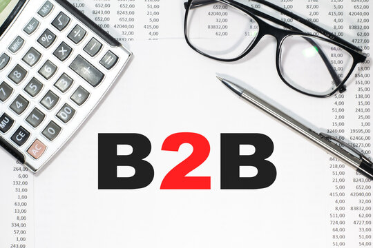 B2B in a magnifying glass on a notepad against the background of graphs, calculator and paper clips.
